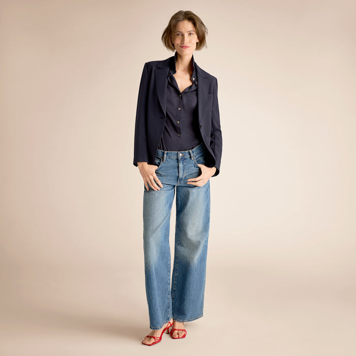 Woman wearing a navy shirt and blue jeans against a beige background