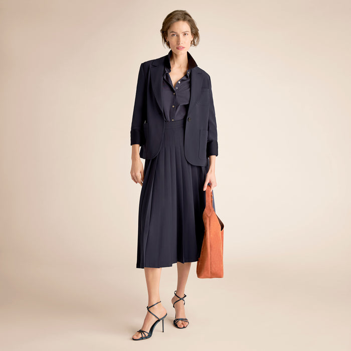 Woman wearing a navy outfit with a brown bag on a beige background