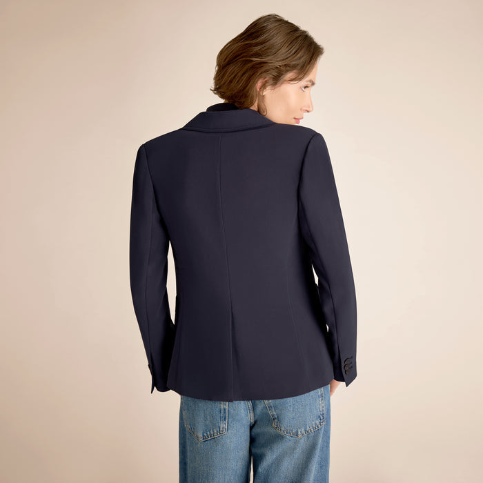 Woman wearing a navy blazer and blue jeans on a beige background