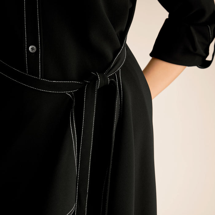 Close-up of a black dress with a tie waist on a beige background