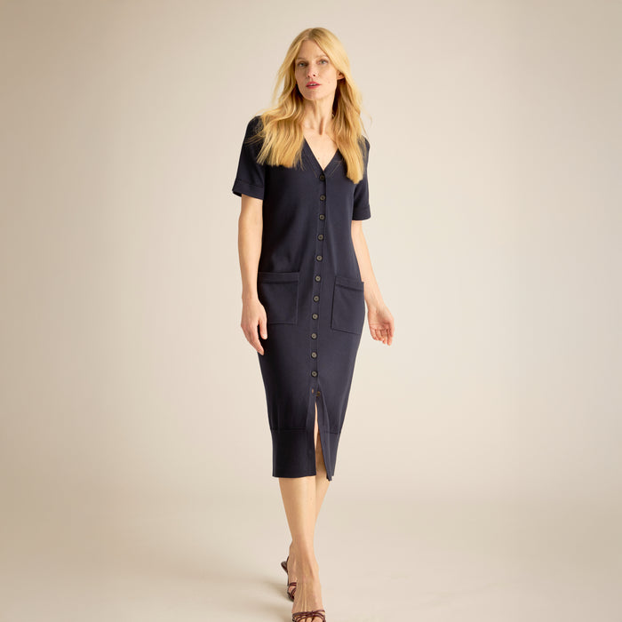 Woman wearing a navy blue dress with a V-neckline and short sleeves on a beige background | Lead