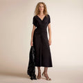 Woman wearing a black dress holding a black sequined jacket against a beige background | Lead