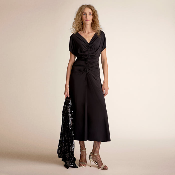 Woman wearing a black dress holding a black sequined jacket against a beige background | Lead