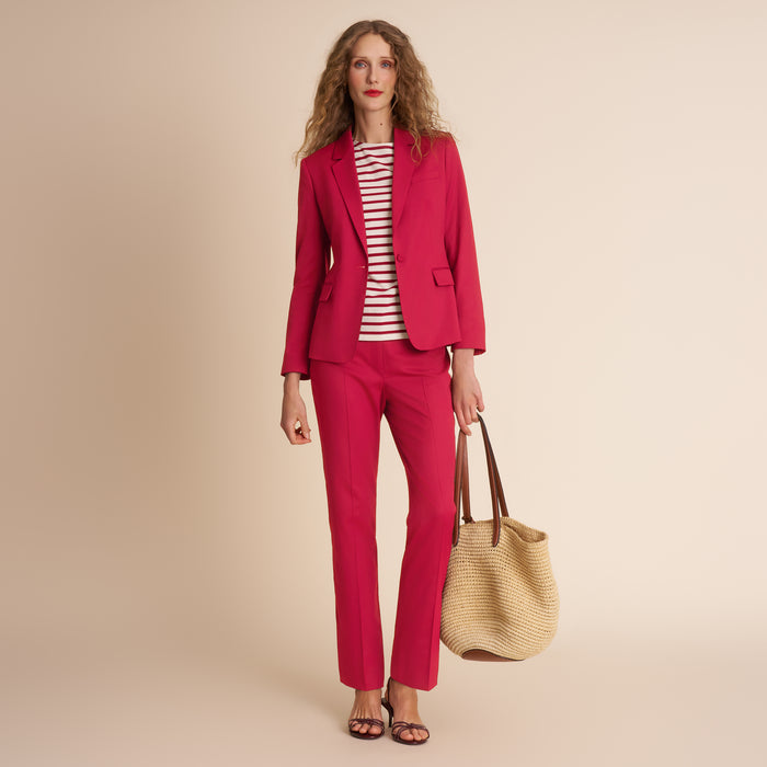 Woman wearing a red suit holding a beige handbag against a beige background | Lead