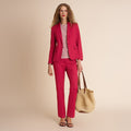 Woman wearing a red suit holding a beige handbag against a beige background | Lead