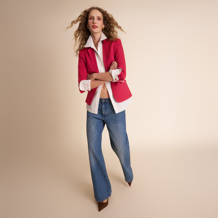 Woman wearing a red blazer, white shirt, and blue jeans on a beige background