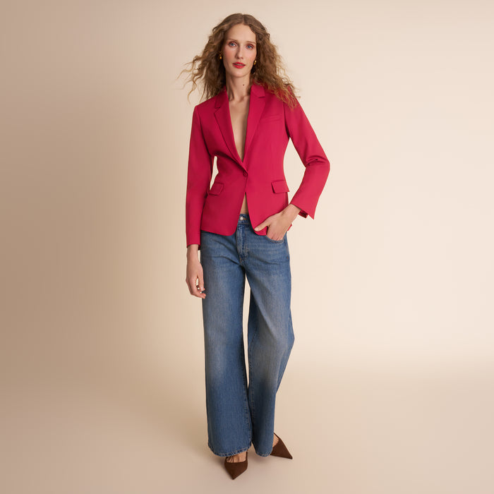Woman wearing a red blazer and blue jeans on a beige background