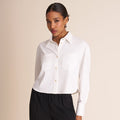 Woman wearing a white shirt and black pants against a beige background | Lead