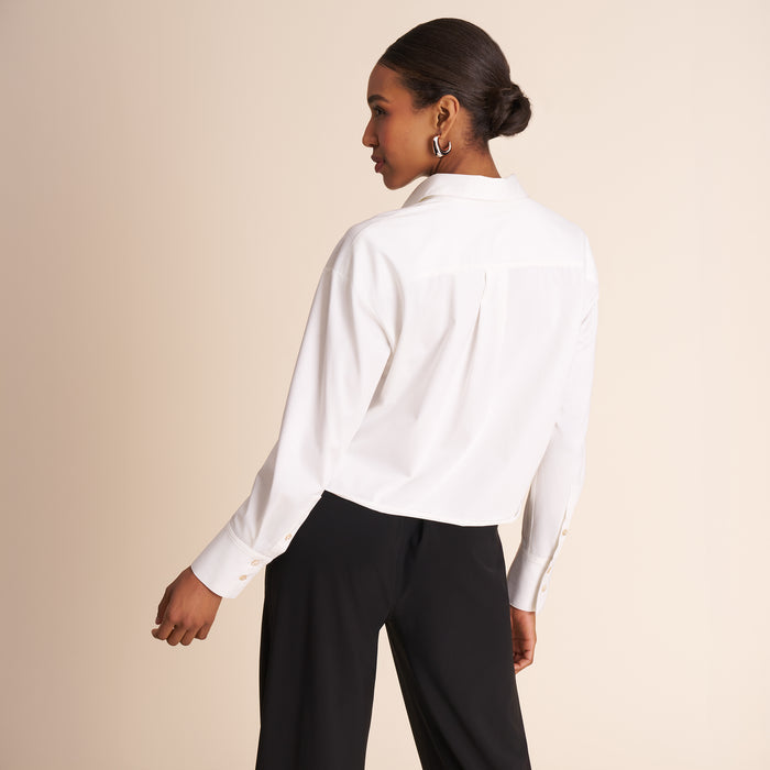 Woman wearing a white blouse and black pants against a beige background