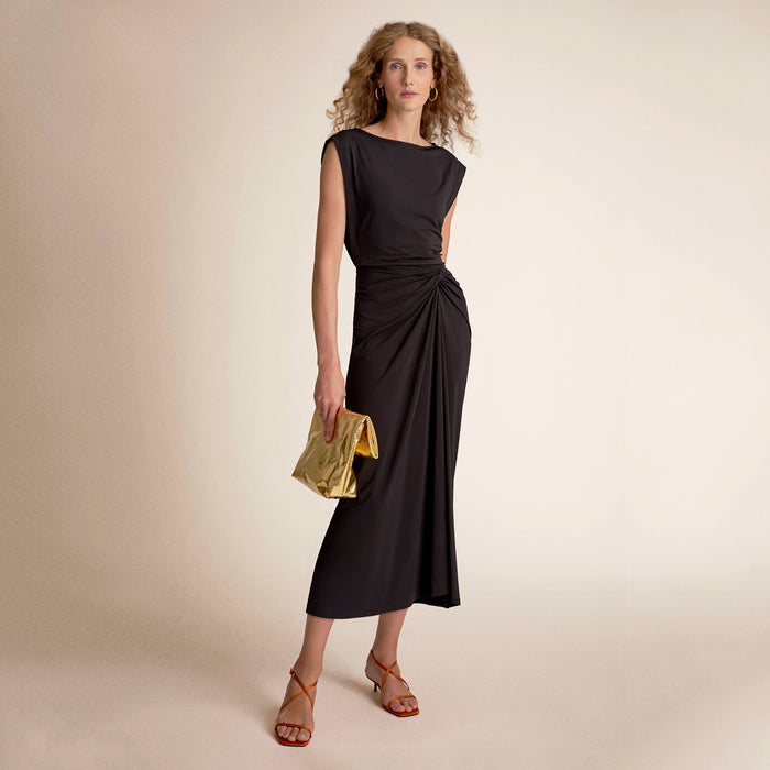 Woman wearing a black dress holding a gold clutch | Lead