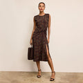Woman wearing a patterned dress with a slit, holding a matching handbag against a beige background. | Lead
