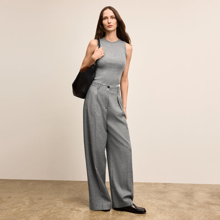 Woman wearing a gray sleeveless top and wide-leg pants holding a black handbag against a beige background