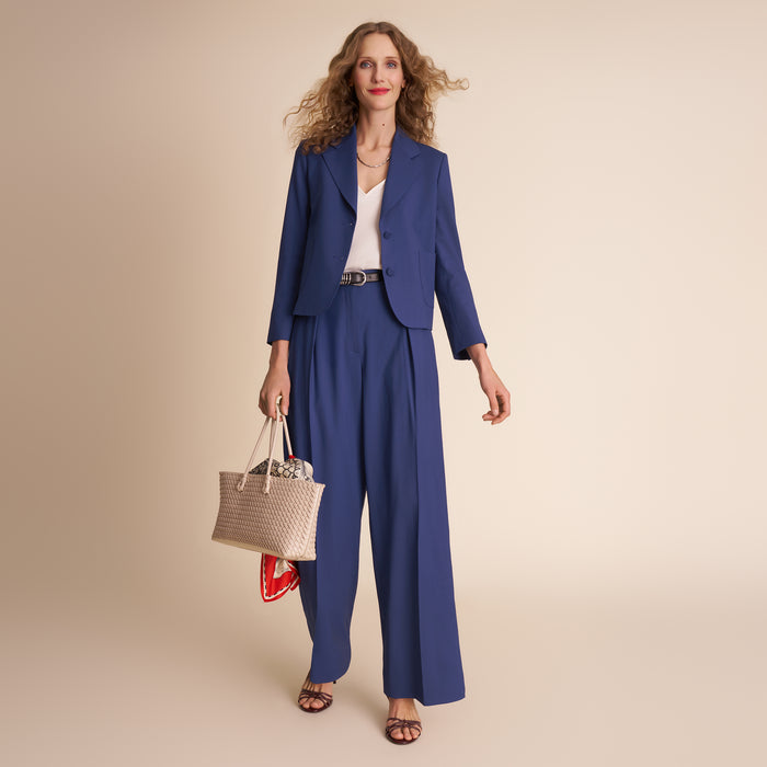 Woman in a blue suit holding a woven bag on a beige background.